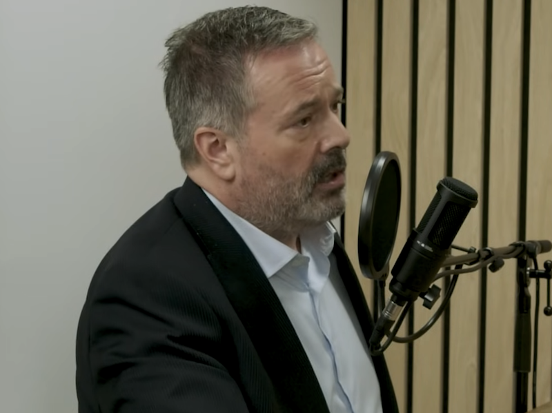 A bearded Jason Kenney speaking at a microphone.