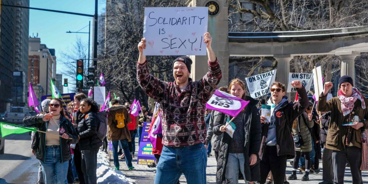 A TA holds up a sign that reads "solidarity is sexy" during a picket.