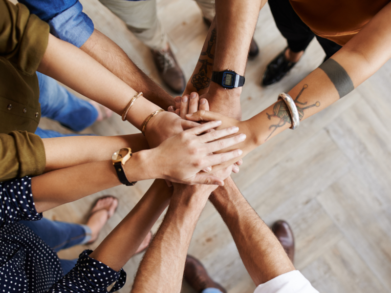 An image of a group of people putting their hands together in a circle.