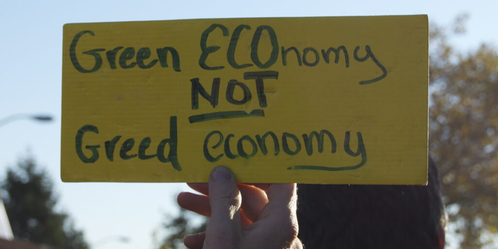 A yellow sign that reads "Green ECOnomy not greed economy."