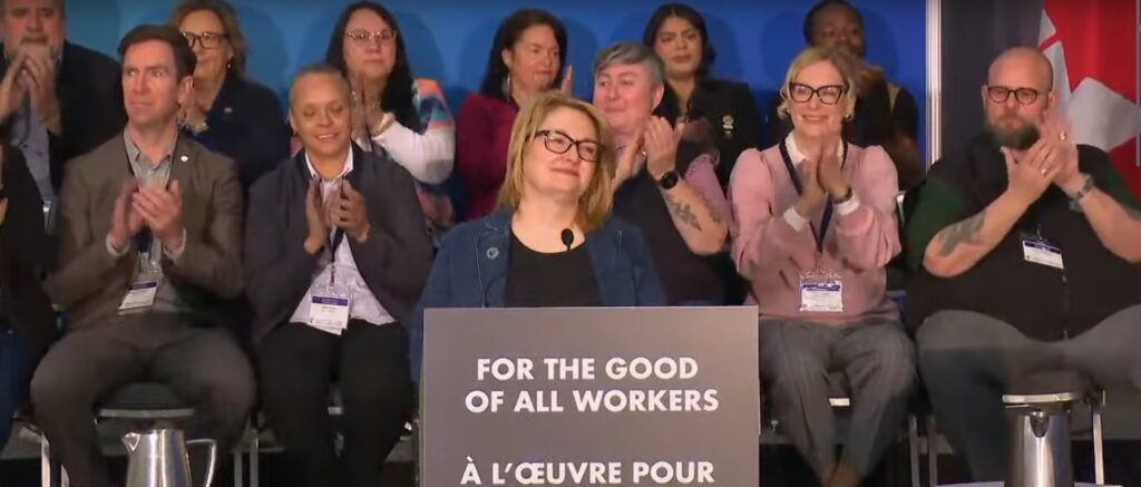 Canadian Labour Congress president Bea Bruske makes a speech on April 18 with labour leaders applauding behind her.