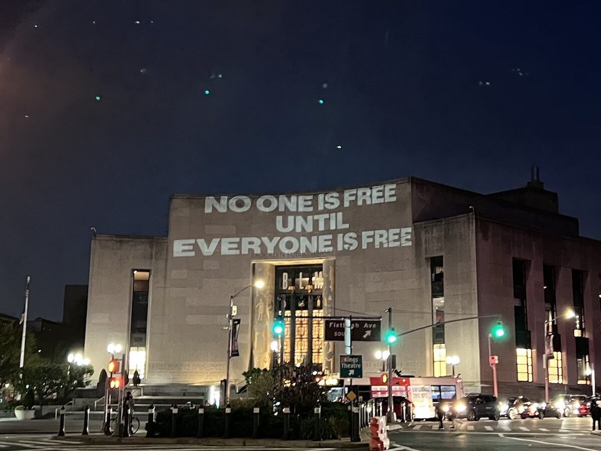 The words "No one is free until everyone is free" projected on the side of a building in New York City.