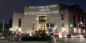 The words "No one is free until everyone is free" projected on the side of a building in New York City.