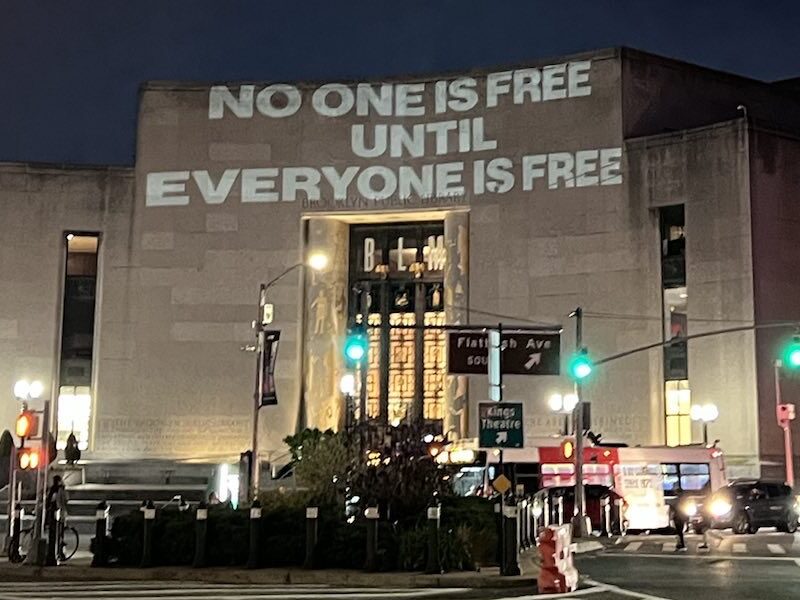 The words "No one is free until everyone is free" projected on the side of a building in New York City.