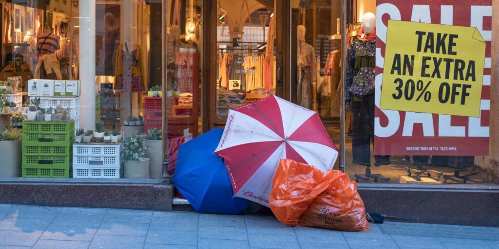 A homeless man camps out in front of a story having a sale.