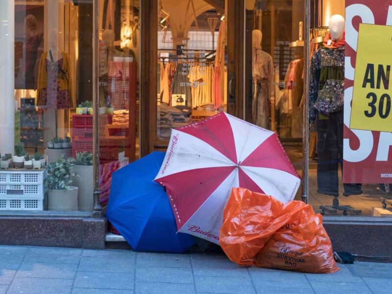 A homeless man camps out in front of a story having a sale.