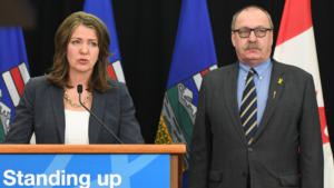 Alberta Municipal Affairs Minister Ric McIver stands next to premier Danielle Smith at a press conference.