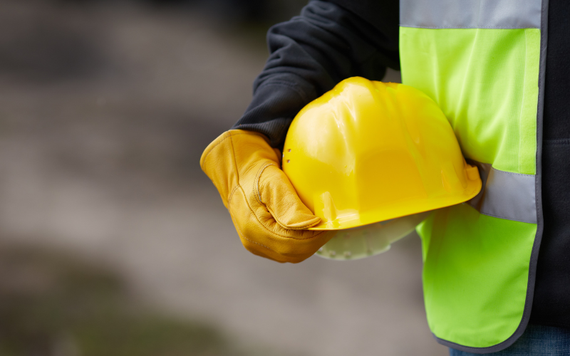 A person in a safety vest holding a safety hat.