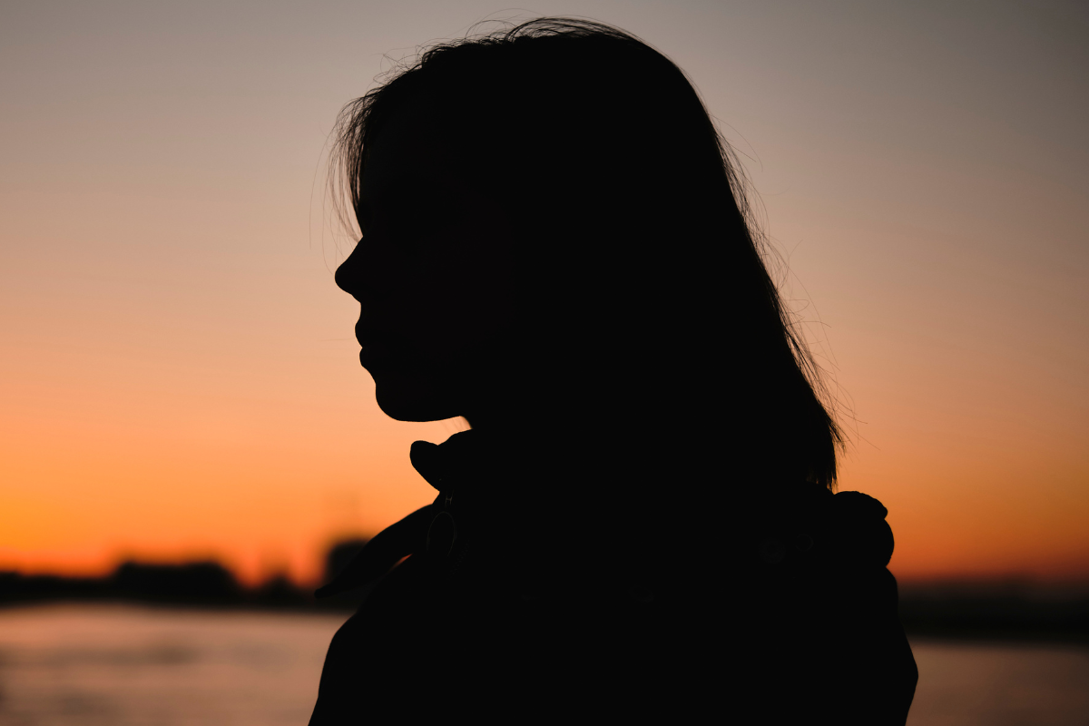 The silhouette of a woman as the sun sets in the background.