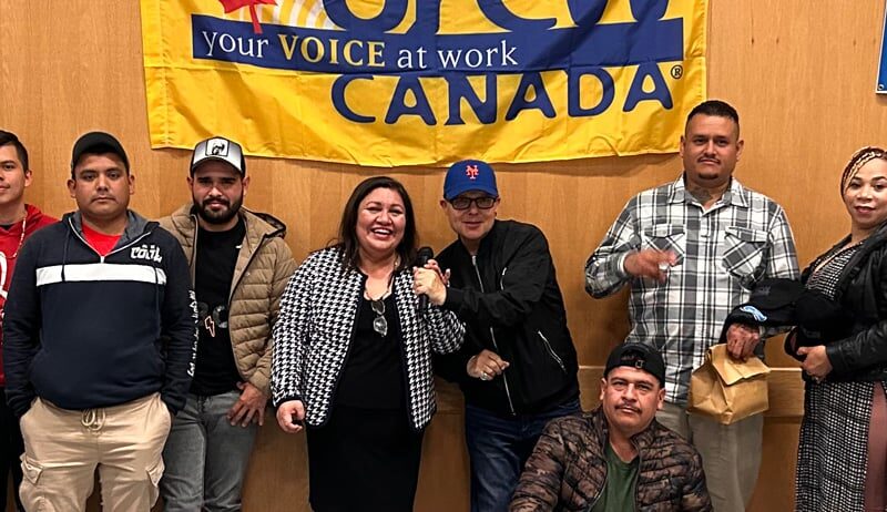 A group of migrant workers smile for a picture. Behind them is a UFCW banner.