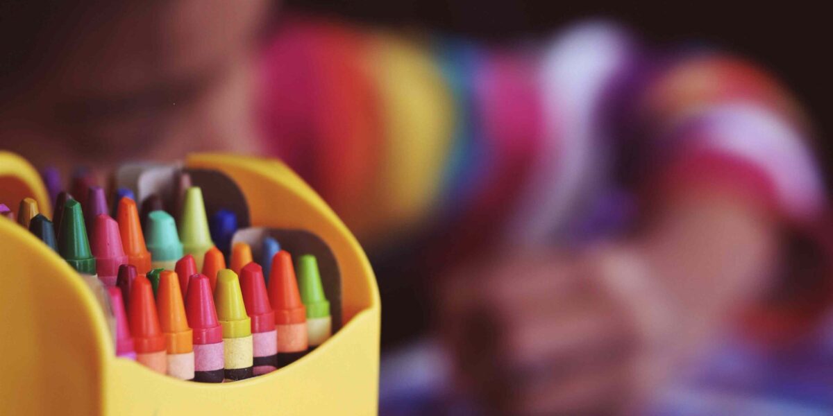 A child colours with a box of crayons in the foreground.