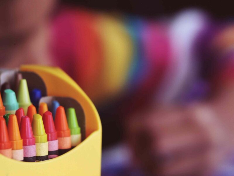 A child colours with a box of crayons in the foreground.