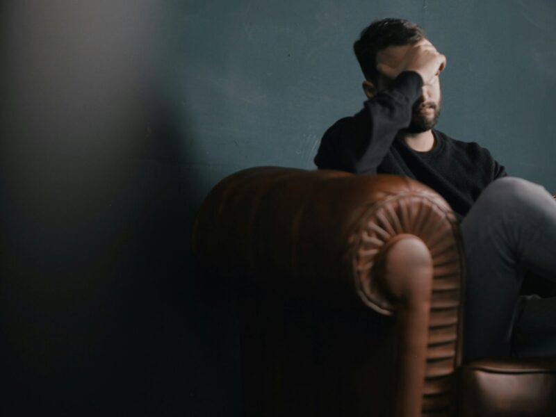 A man sits on a couch with his face in his hand.