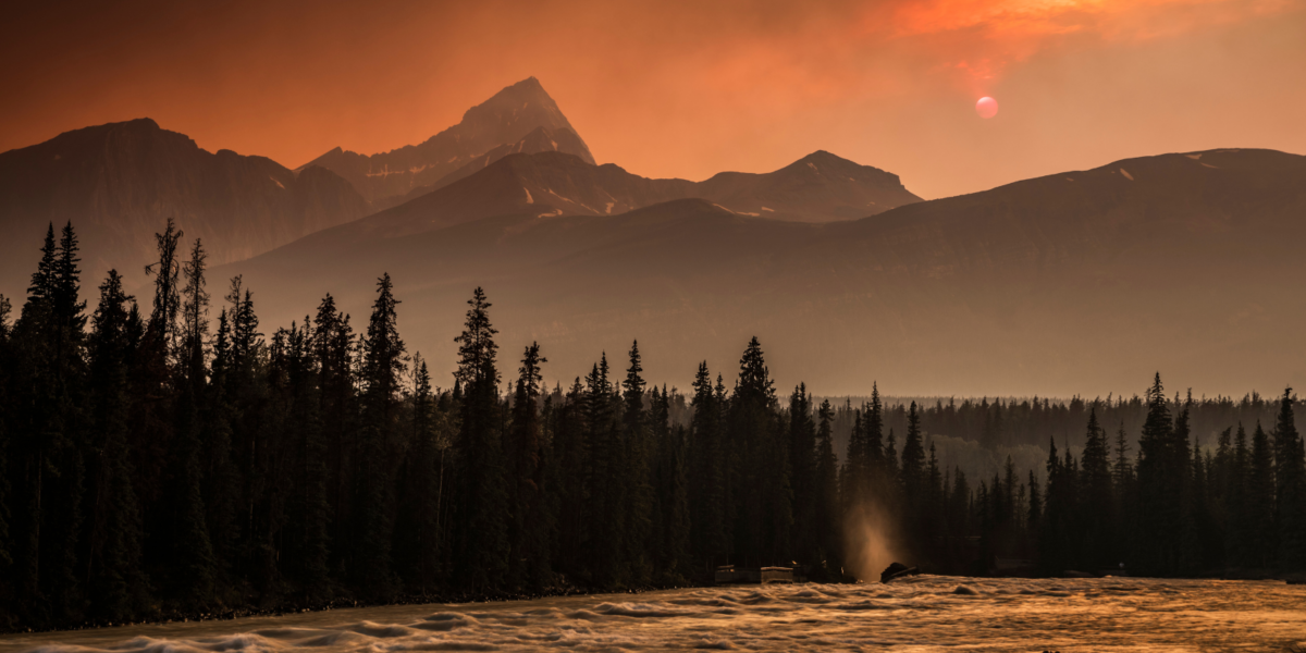 A photo of an orange, smoky sky over a mountain landscape.