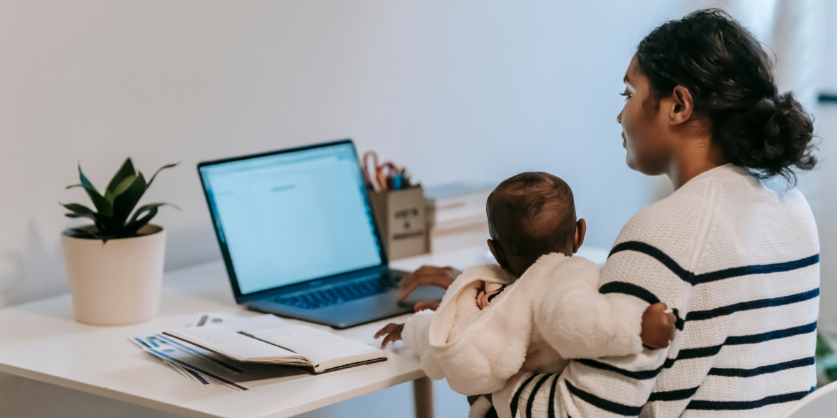 A person sitting at a desk with a baby in their arms.