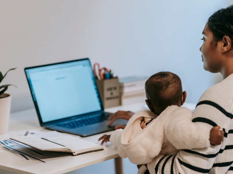 A person sitting at a desk with a baby in their arms.