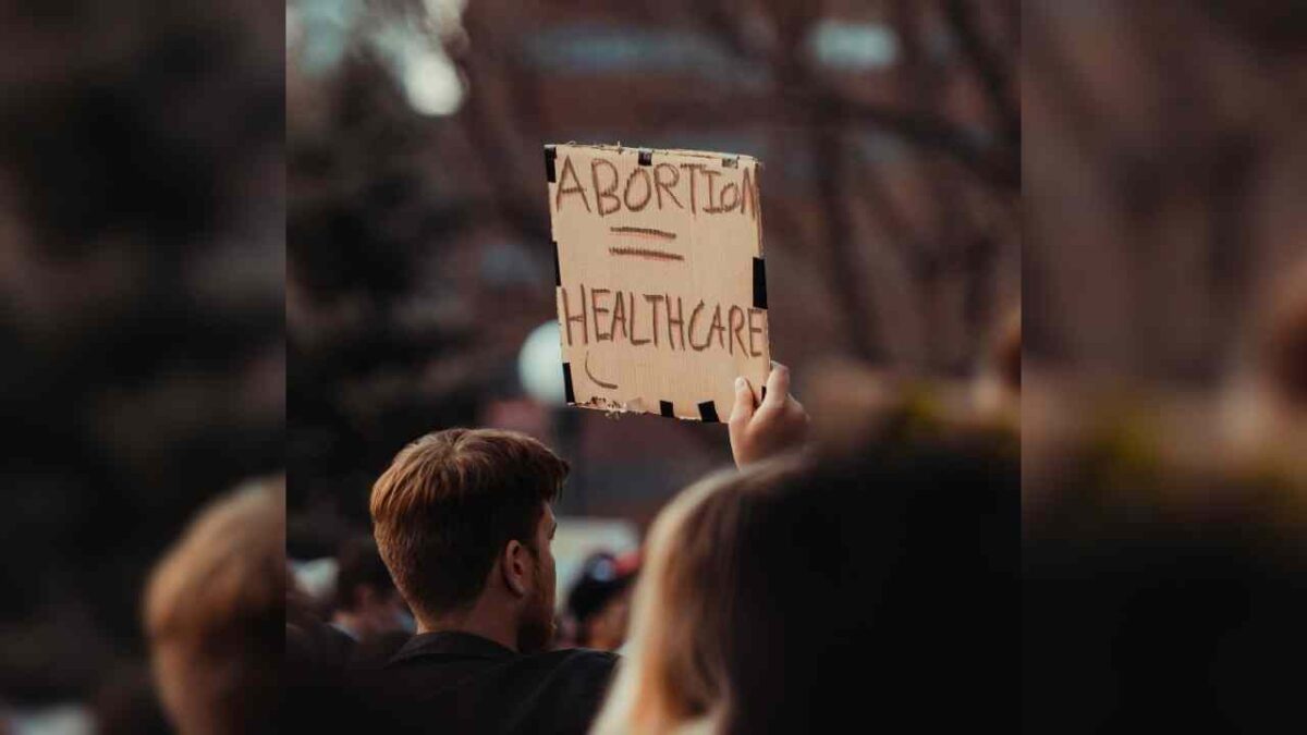 A man at a protest holding a sign that reads Abortion = healthcare.