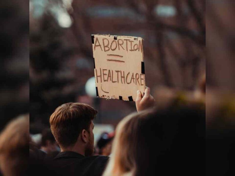 A man at a protest holding a sign that reads Abortion = healthcare.