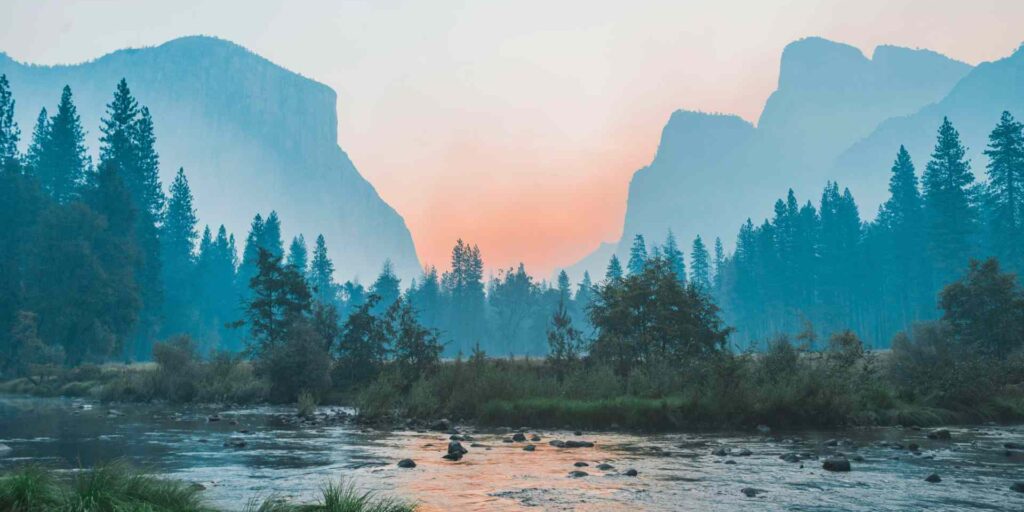 A stream at dawn, with a forest and mountains in the background.