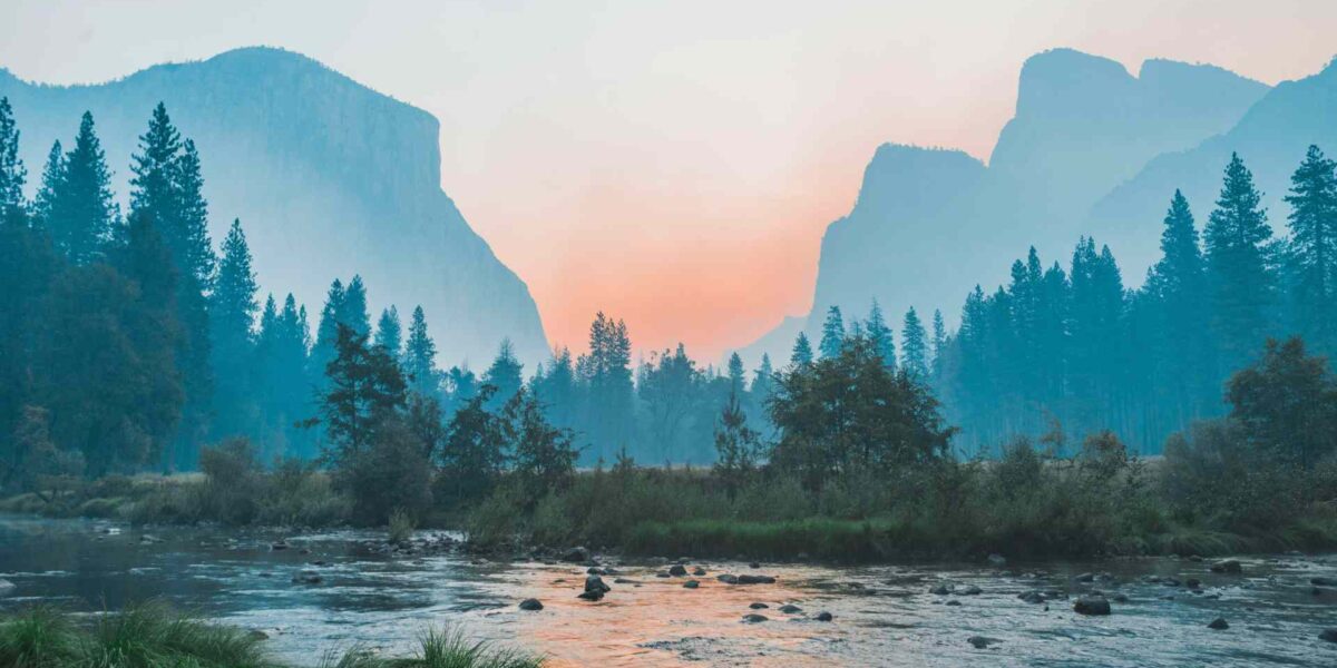 A stream at dawn, with a forest and mountains in the background.