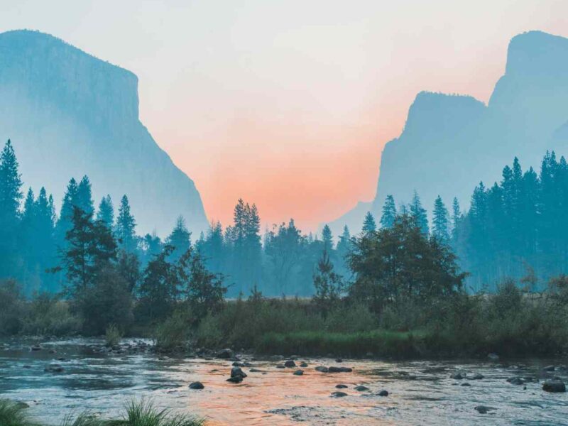 A stream at dawn, with a forest and mountains in the background.