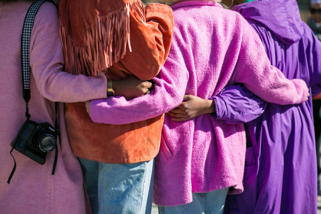 The back of four people in coloured coats holding each others hands.