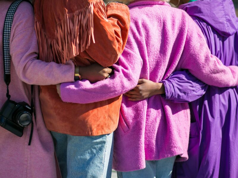 The back of four people in coloured coats holding each others hands.