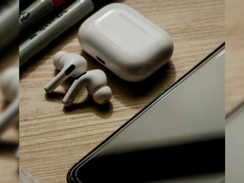 A cellphone on a desk along with earbuds and markers.