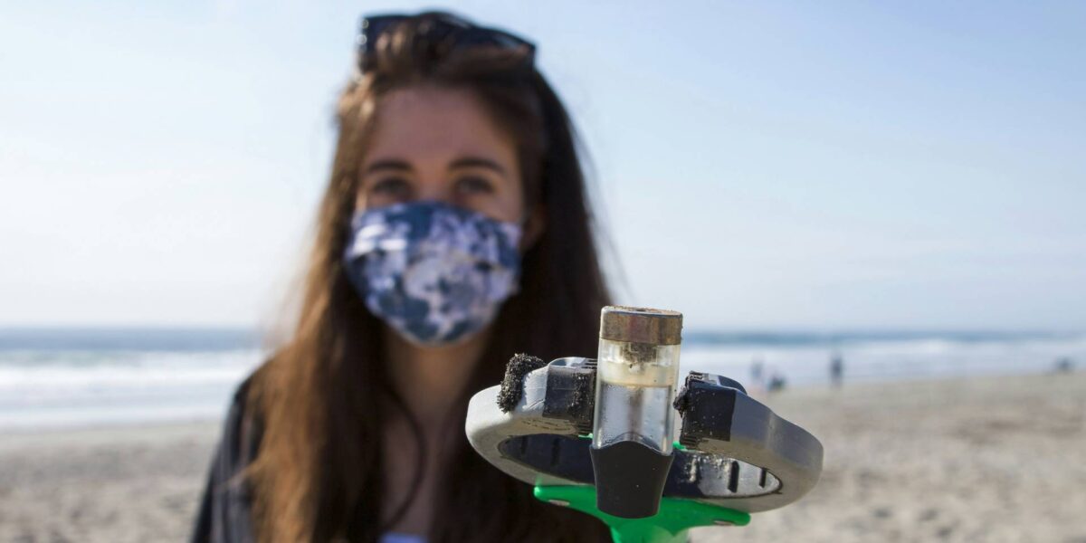 A woman collects plastic from a beach with a grabbing arm.