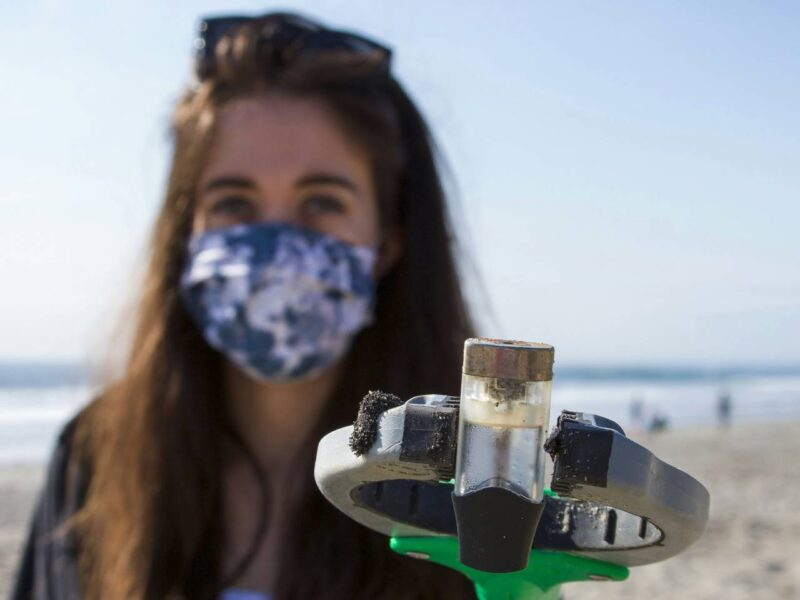 A woman collects plastic from a beach with a grabbing arm.