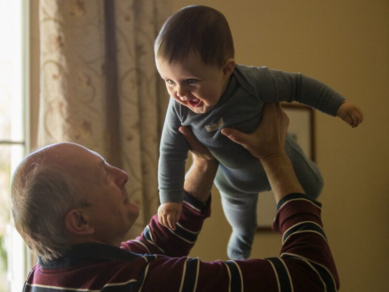 A grandfather lifts his grandchild up in the air.