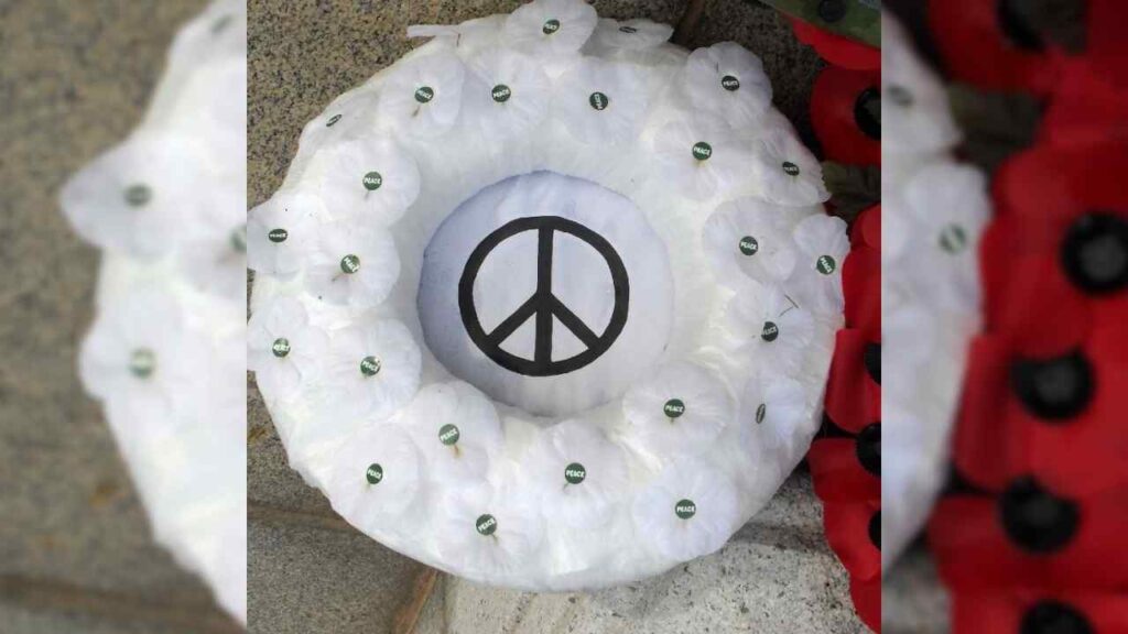 A white poppy wreath with a peace symbol at its centre.