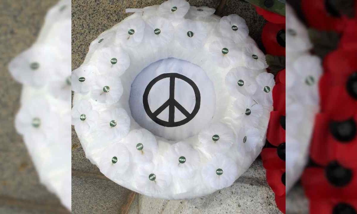 A white poppy wreath with a peace symbol at its centre.