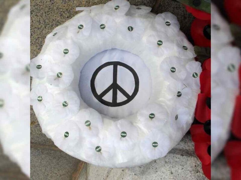 A white poppy wreath with a peace symbol at its centre.