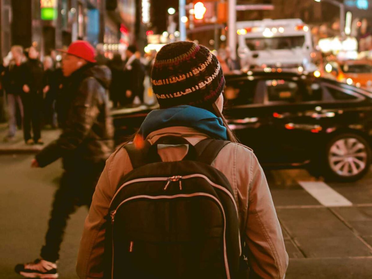 A woman with a backpack crossing a busy city street at night.