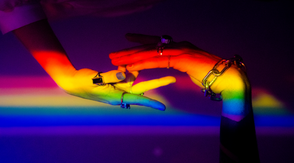 Two hands under rainbow light, indicating pride.