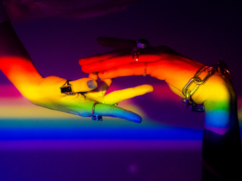 Two hands under rainbow light, indicating pride.