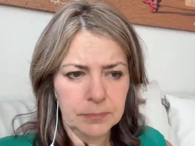 Alberta Premier Danielle Smith, cranky, propped up by pillows, but not in bed, during her virtual news conference from an undisclosed location in the United States.