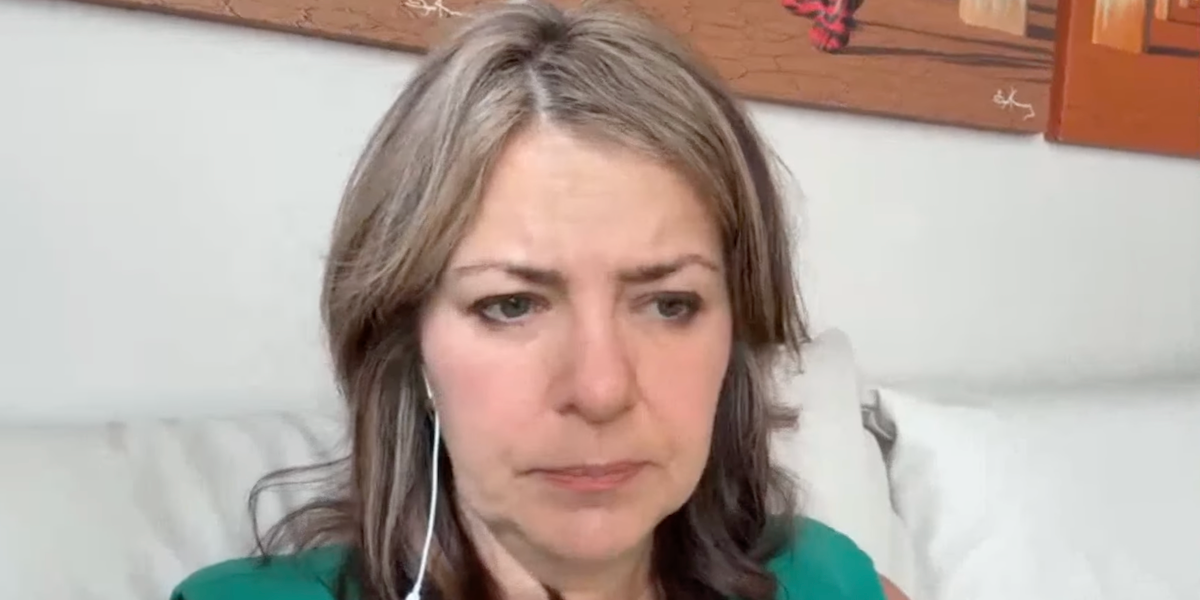 Alberta Premier Danielle Smith, cranky, propped up by pillows, but not in bed, during her virtual news conference from an undisclosed location in the United States.