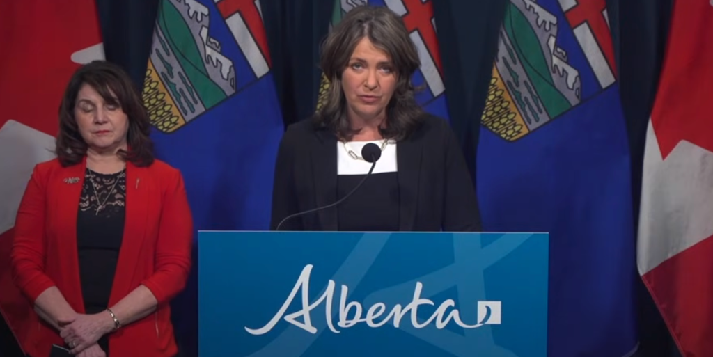 Alberta Premier Danielle Smith talks at a news conference with her health minister, Adriana LaGrange in the background.