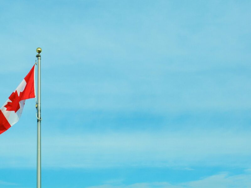 An image of a Canadian flag in front of a clear blue sky. PSAC is calling out the Canadian government for cuts to frontline staff at IRCC.