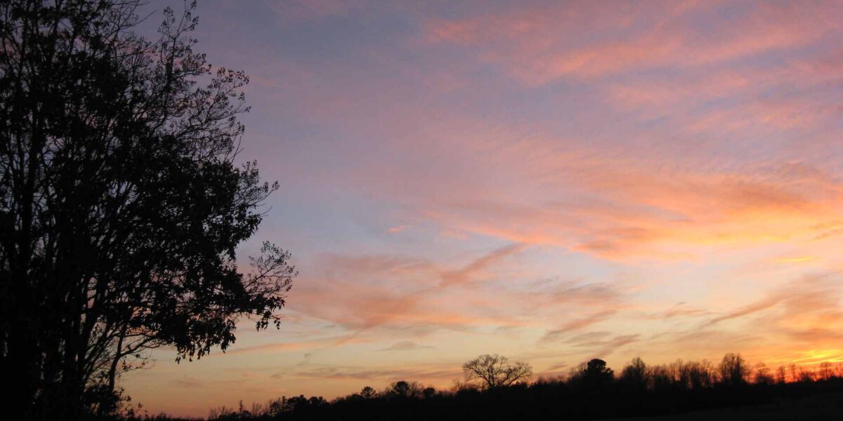 A setting sun with a purple sky and a landscape in a black silhouette.