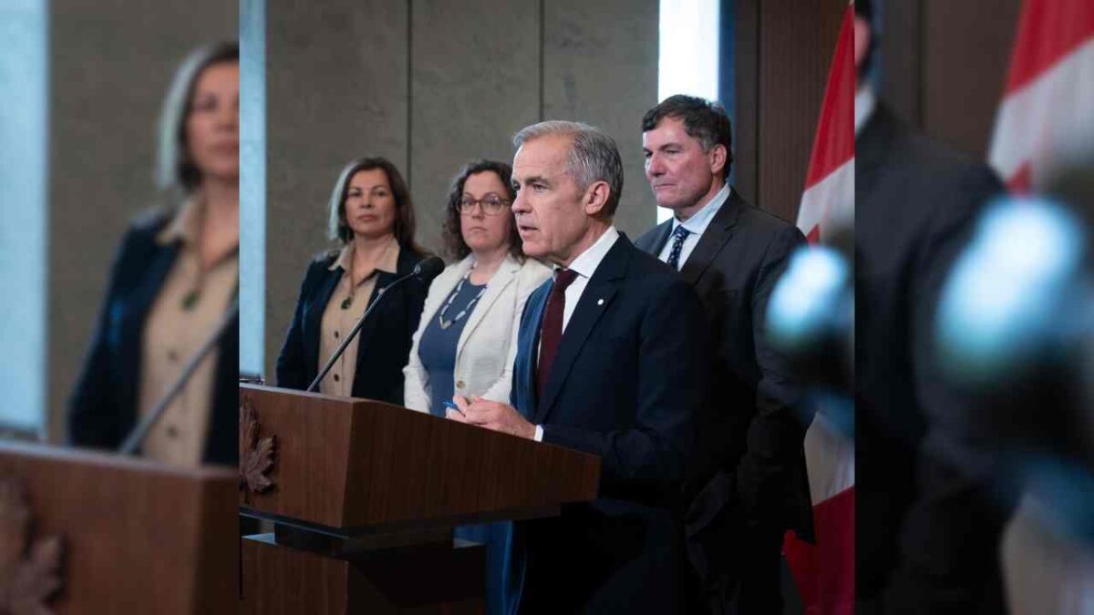 Mark Carney holding a press conference on his One Canadian Economy Act with minister Dominic Leblanc in the background.