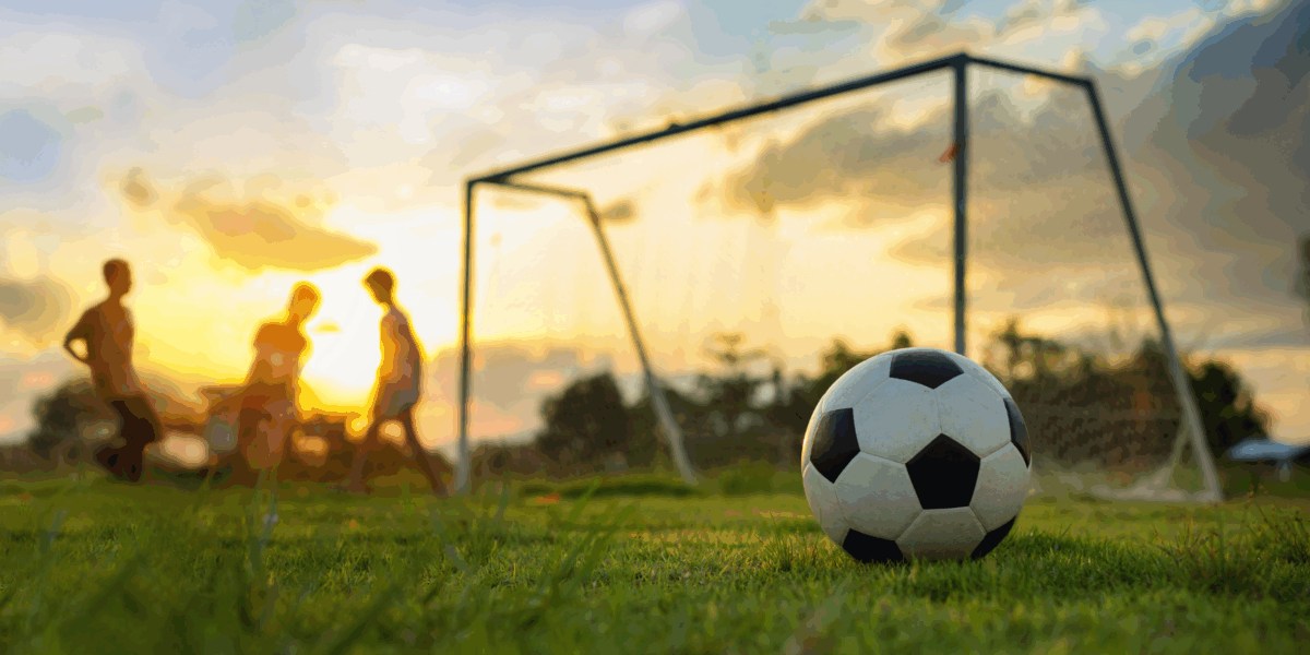A trio of children playing on a field with a soccer ball in the foreground.
