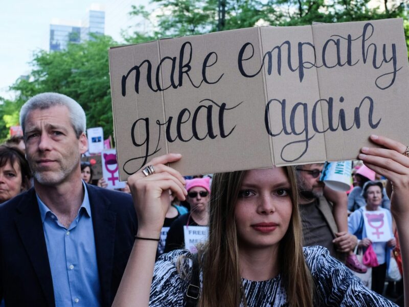 A woman holds a sign reading "make empathy great again."