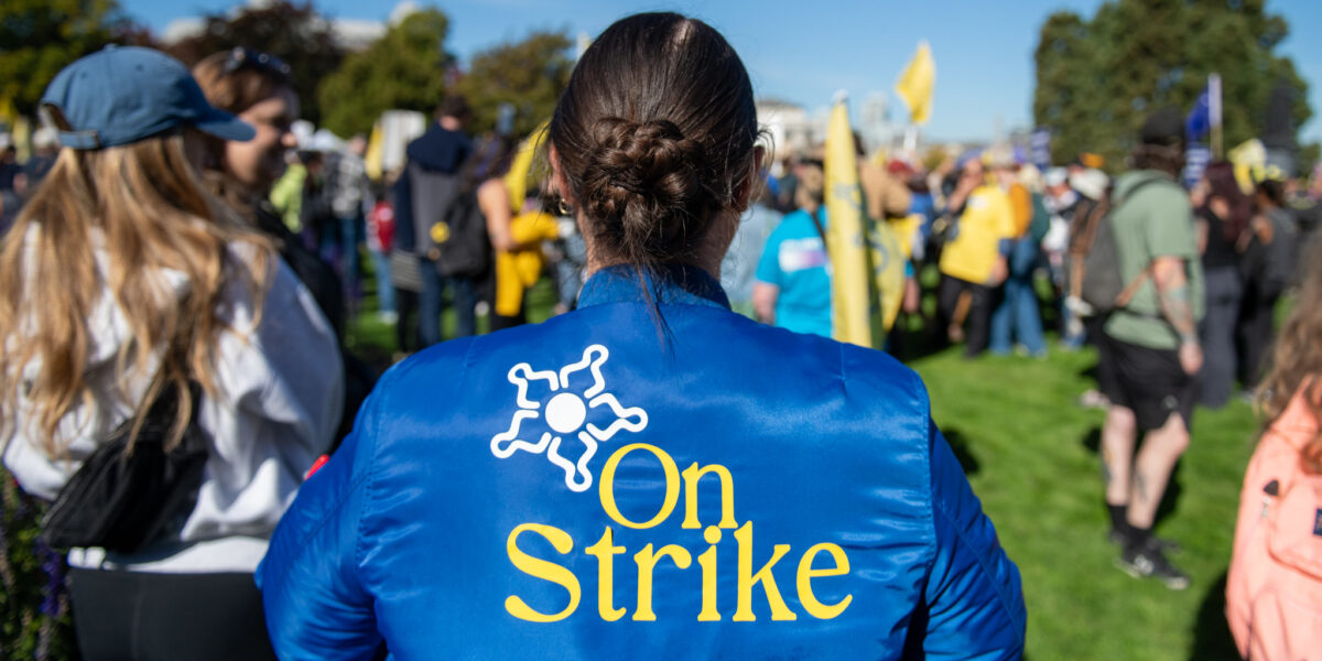 A BCGEU member wearing a blue jacket that reads "On Strike."
