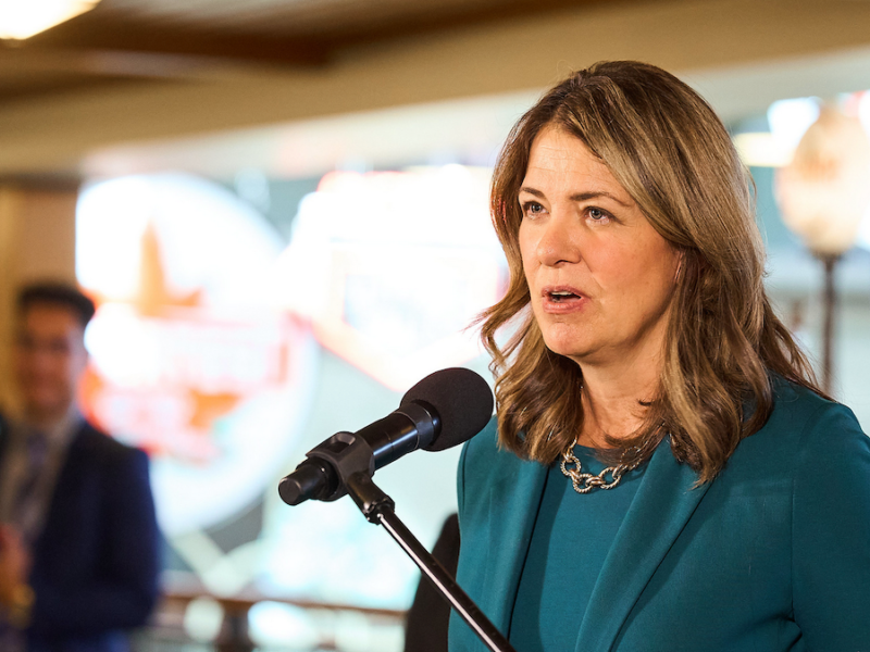 Alberta Premier Danielle Smith at an unrelated recent event, with her press secretary hovering in the background.