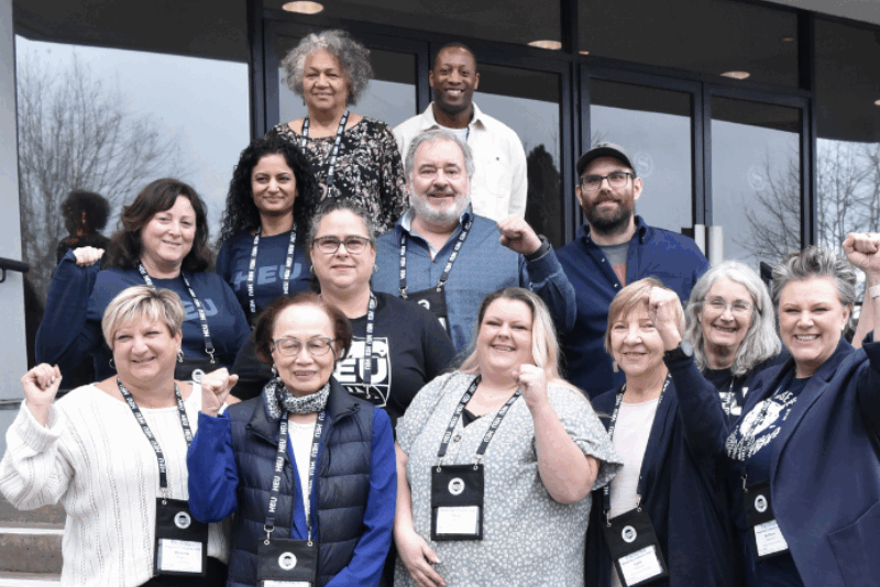 An image of the HEU FBA standing on the steps of the a building raising their fists. The FBA has reached a tentative agreement.