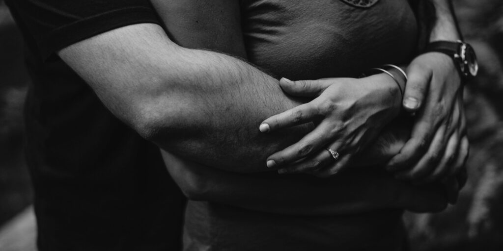 A man hugs a woman from behind in black and white.