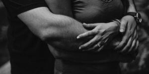A man hugs a woman from behind in black and white.
